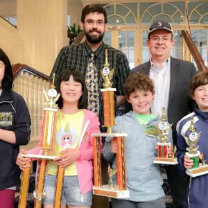 Group of children holding trophies, smiling indoors.